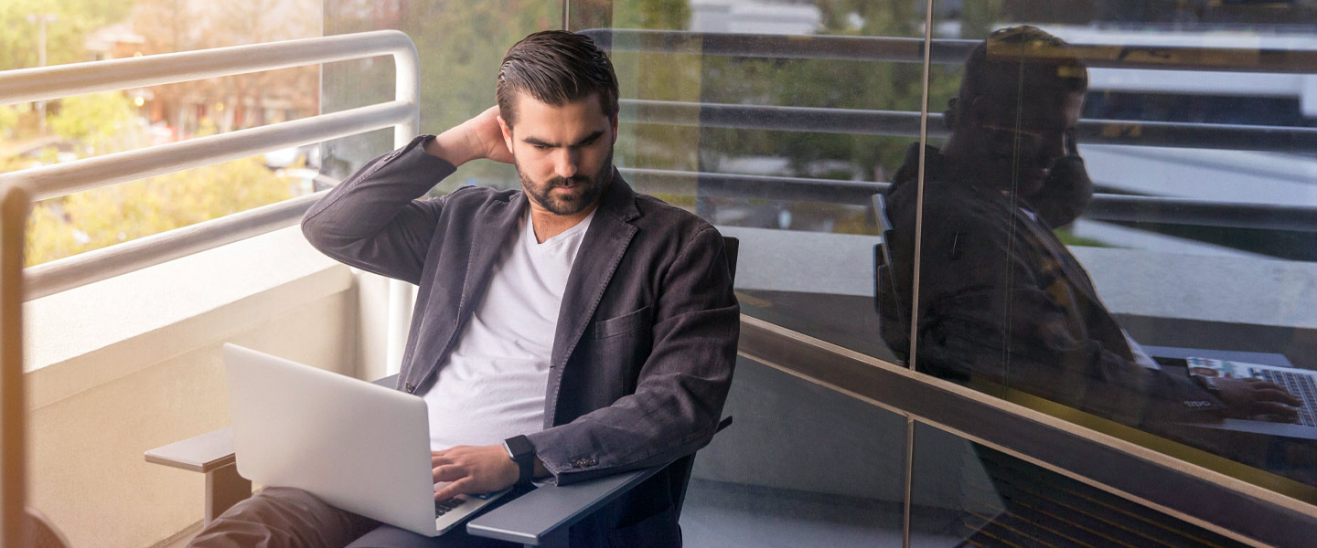 Mann sitzt mit Laptop auf seiner Terrasse.