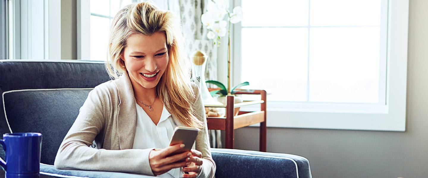 Blonde Frau schaut lachend auf ihr Samsung Smartphone